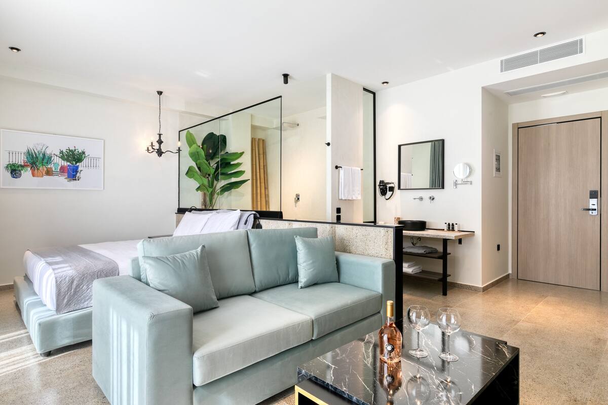 A modern hotel room with a bed, a light blue sofa, a marble coffee table, and a large mirror.