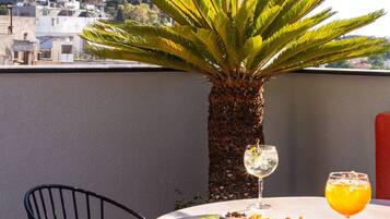 A round table with a white tablecloth, two chairs, a palm tree, and a glass of orange juice.