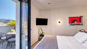 Ein Hotelzimmer mit Bett, einem an der Wand befestigten Fernseher, einem kleinen Tisch mit Stühlen und Blick auf die Stadtlandschaft.