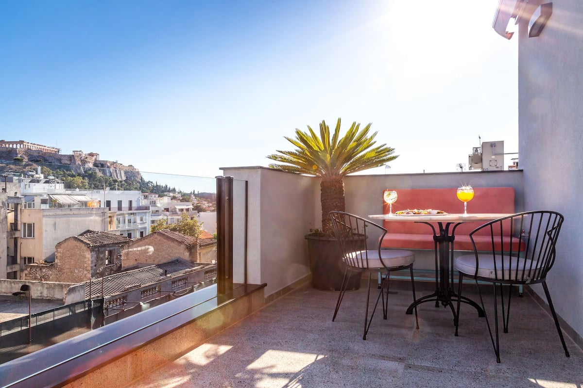 A balcony with a table and chairs, a potted plant, and a view of the cityscape.