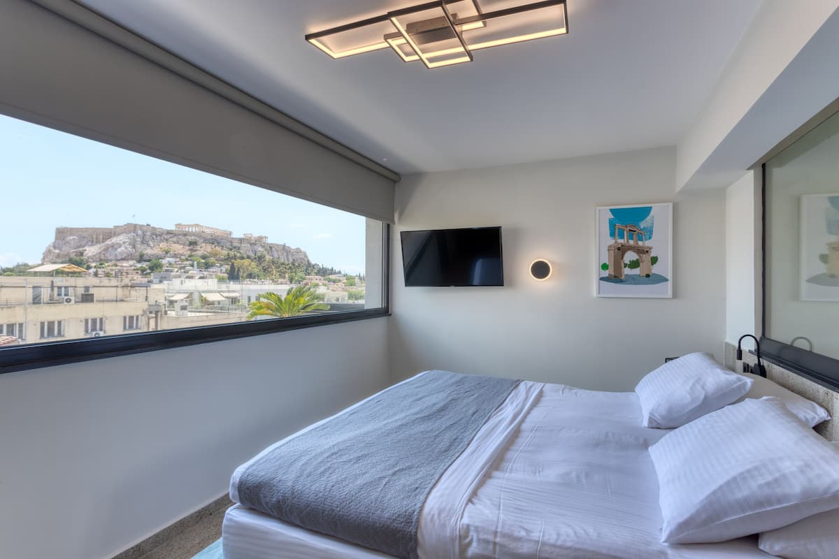 A modern hotel room with a large bed, a flat-screen TV, a view of a historic building, and a framed picture on the wall.