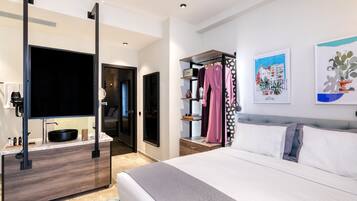 A modern hotel room with a large bed, a TV mounted on a cabinet, a walk-in closet, and artwork on the walls.
