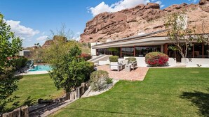 Una casa moderna con piscina, un patio con mobiliario exterior y montañas al fondo.