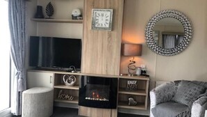 Una sala de estar acogedora con una televisión de pantalla plana, una chimenea, un espejo redondo y un sofá cómodo.