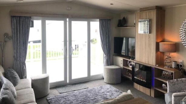 Una sala de estar moderna con sofá, reposapiés, televisor y mueble de entretenimiento.