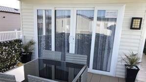 Un patio con una mesa de vidrio y sillas de mimbre, una puerta corredera de vidrio y plantas en macetas.