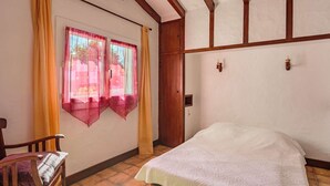 A bedroom with a bed, wooden chair, and a window with curtains. - Cozy Ground Floor Apartment Near Erromardie Beach, Terrace & Parking (Saint-Jean-de-Luz)