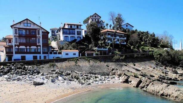 A coastal area with buildings on a hillside, a rocky shoreline, and clear water. - Cozy Ground Floor Apartment Near Erromardie Beach, Terrace & Parking (Saint-Jean-de-Luz)