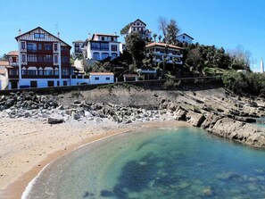 Eine Küstenlandschaft mit Gebäuden an einem Hügelhang, felsigem Ufer und klarem Wasser.