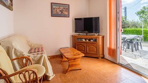 A living room with a sofa, chairs, a wooden coffee table, a television on a wooden stand, and a large window with curtains. - Cozy Ground Floor Apartment Near Erromardie Beach, Terrace & Parking (Saint-Jean-de-Luz)