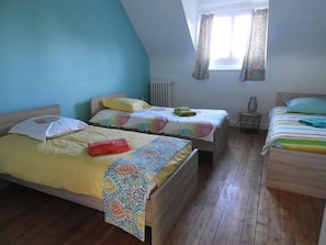 A room with two beds, wooden flooring, and a window with patterned curtains.