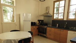 A kitchen with a stove, oven, and refrigerator. There is a dining table with chairs. - Charming Cottage Near Le Mans: Garden, Terrace, 4 Bedrooms, 3 Bathrooms, Wi-Fi, Family Friendly (Écommoy)
