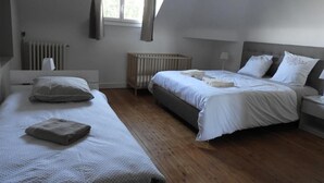 A bedroom with two beds, a window, a radiator, and a crib. - Charming Cottage Near Le Mans: Garden, Terrace, 4 Bedrooms, 3 Bathrooms, Wi-Fi, Family Friendly (Écommoy)