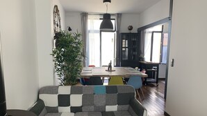 A cozy living room with a sofa, a dining table with chairs, a potted plant, and a bookshelf. - Charming Beach House, Sleeps 10, 150m from Shore (Fort-Mahon-Plage)
