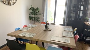 A dining area with a wooden table, colorful chairs, and a potted plant. - Charming Beach House, Sleeps 10, 150m from Shore (Fort-Mahon-Plage)