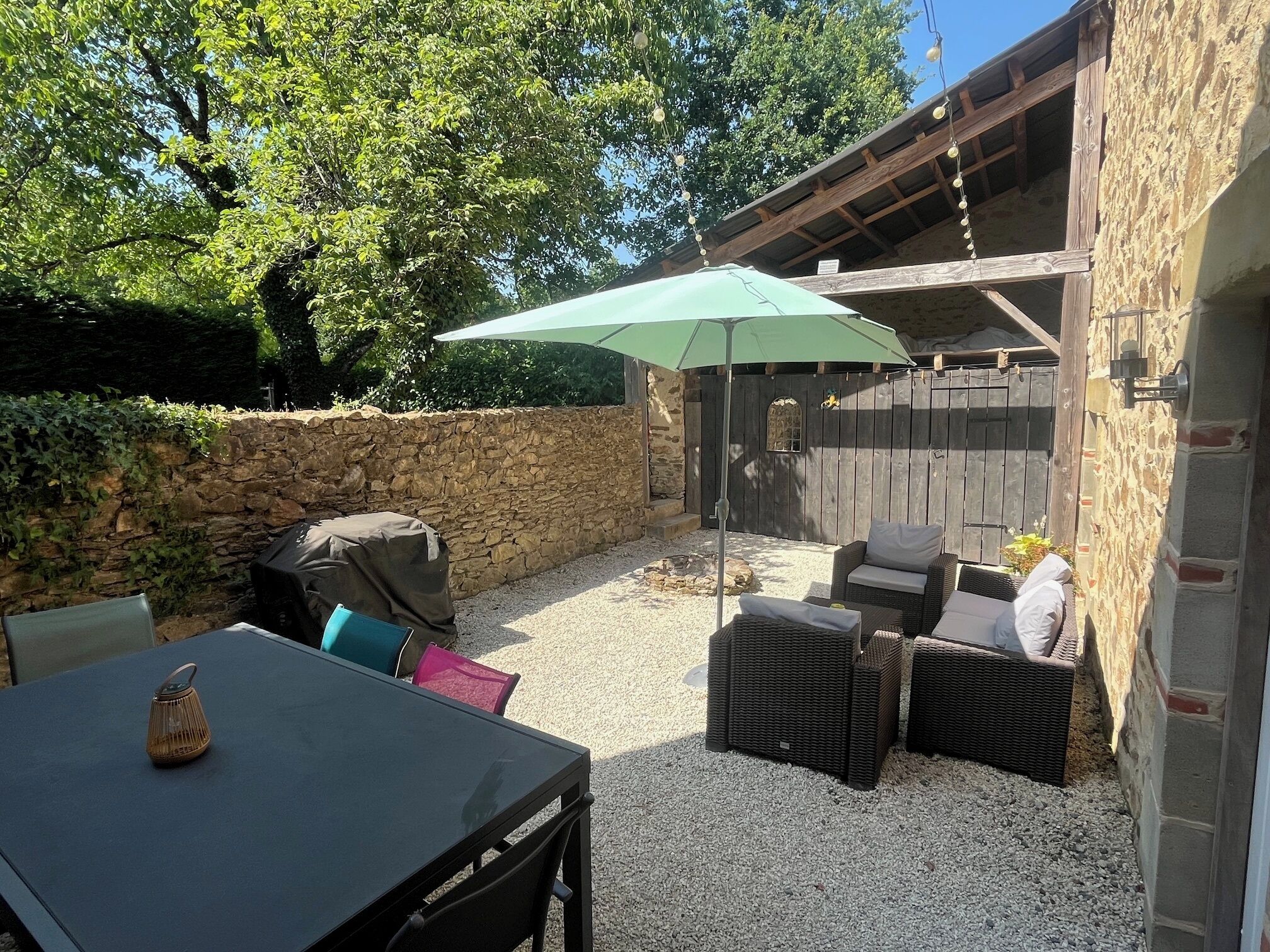 Een terras buiten met een tafel, stoelen en een overdekt zitgedeelte.
