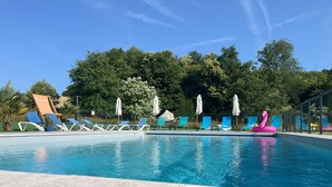 Piscina con sillones de descanso y sombrillas, rodeada de árboles.