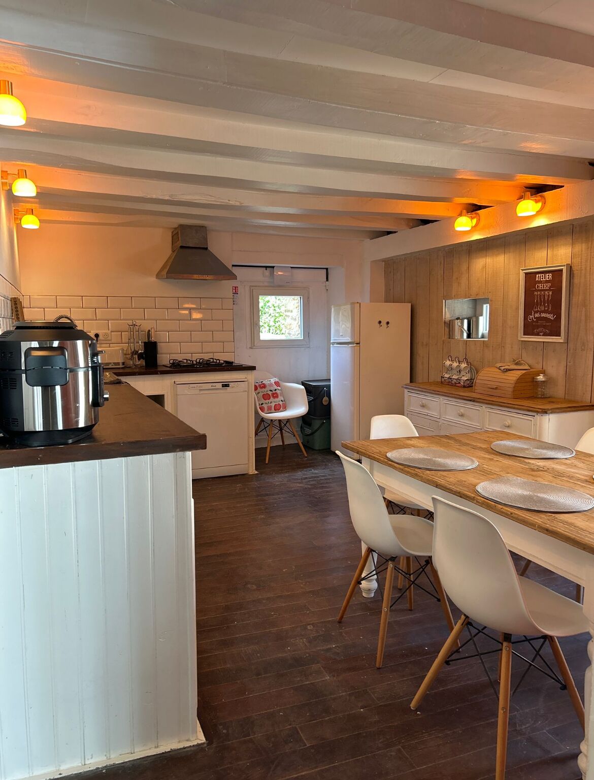 Una cocina compacta con una isla central, un comedor con mesa de madera y vista al espacio de sala.