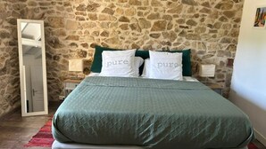 Una cama con una colcha verde y dos almohadas con la palabra "pure" bordada, frente a una pared de piedra.
