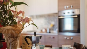 Una cocina con una cafetera sobre una mesa de madera, un florero y una taza.