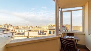 Un balcón con mesa y sillas, con vista a un paisaje urbano con varios edificios.