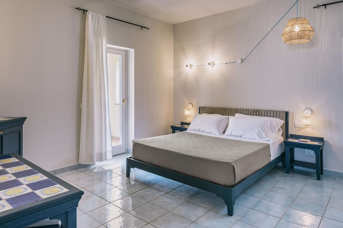 A bedroom with a bed, bedside tables, a nightstand, a lamp, and a window with curtains.