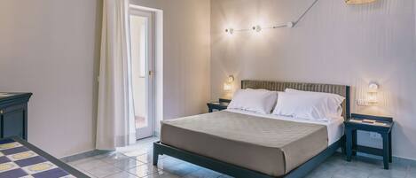 A bedroom with a bed, bedside tables, a nightstand, a lamp, and a window with curtains.