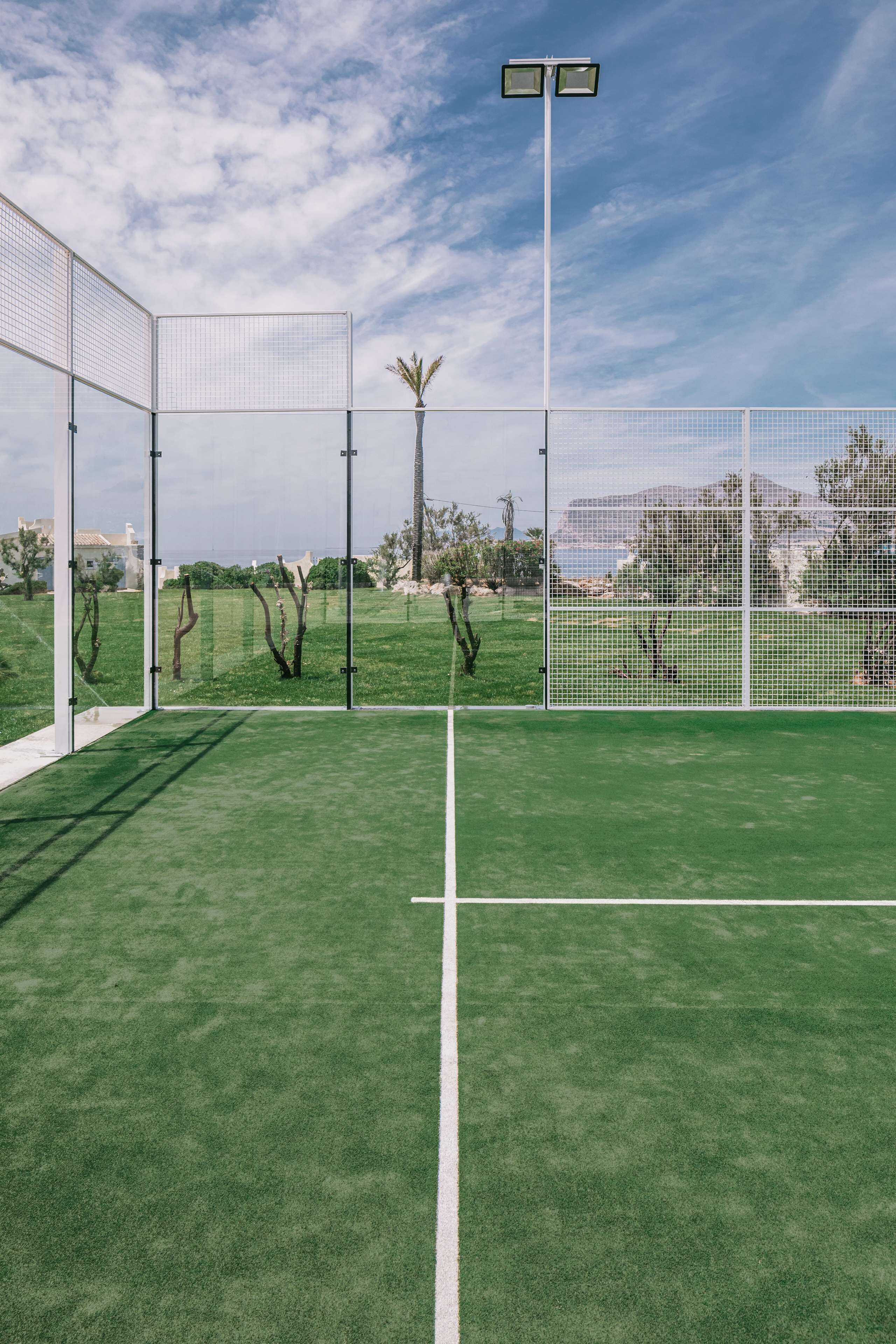 Cancha deportiva al aire libre con césped artificial, rodeada por una valla blanca, bajo cielos despejados.