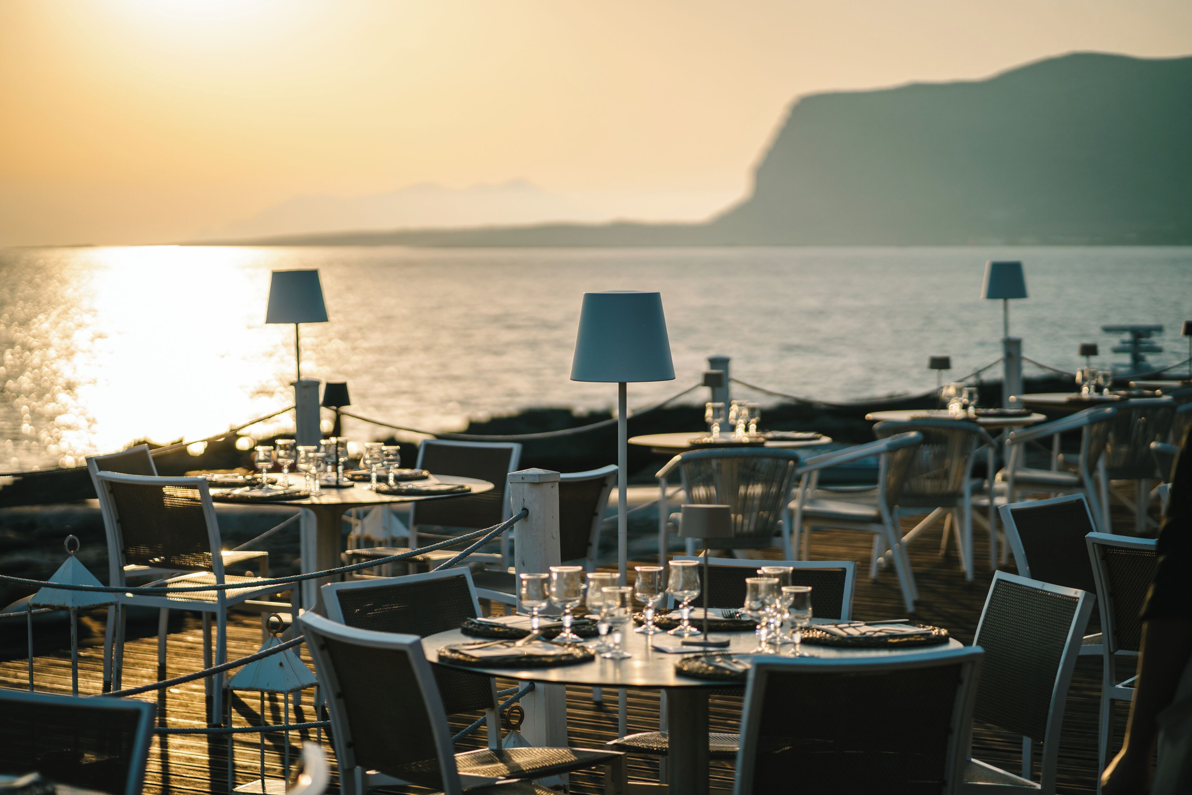 A seaside restaurant with tables and chairs arranged for dining, overlooking the ocean.