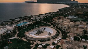 An aerial view of a coastal resort with a swimming pool, amphitheater, and Mediterranean-style buildings. - Mangia's Favignana Resort (Favignana)