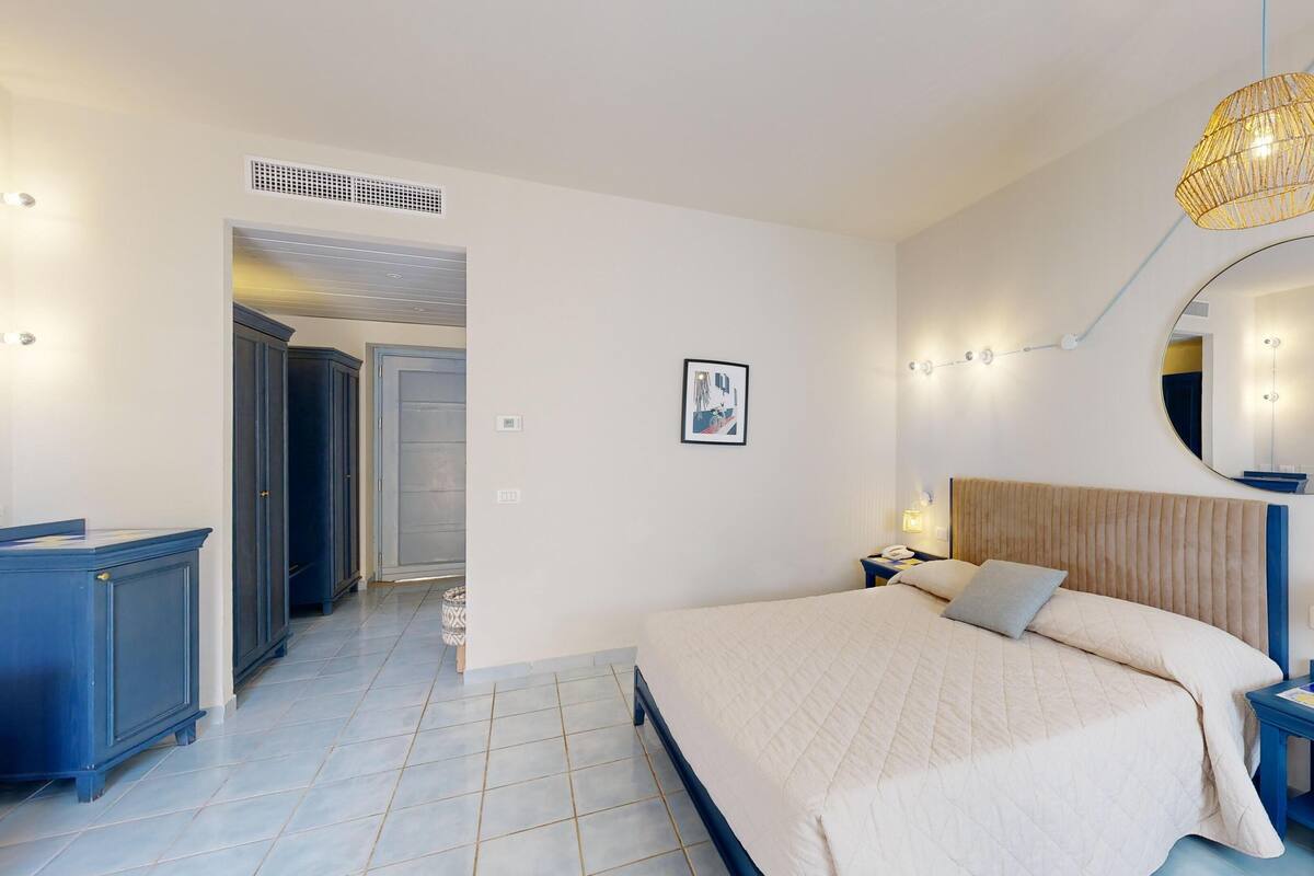 A modern bedroom with a large bed, a bedside table, a mirror, and a wardrobe.