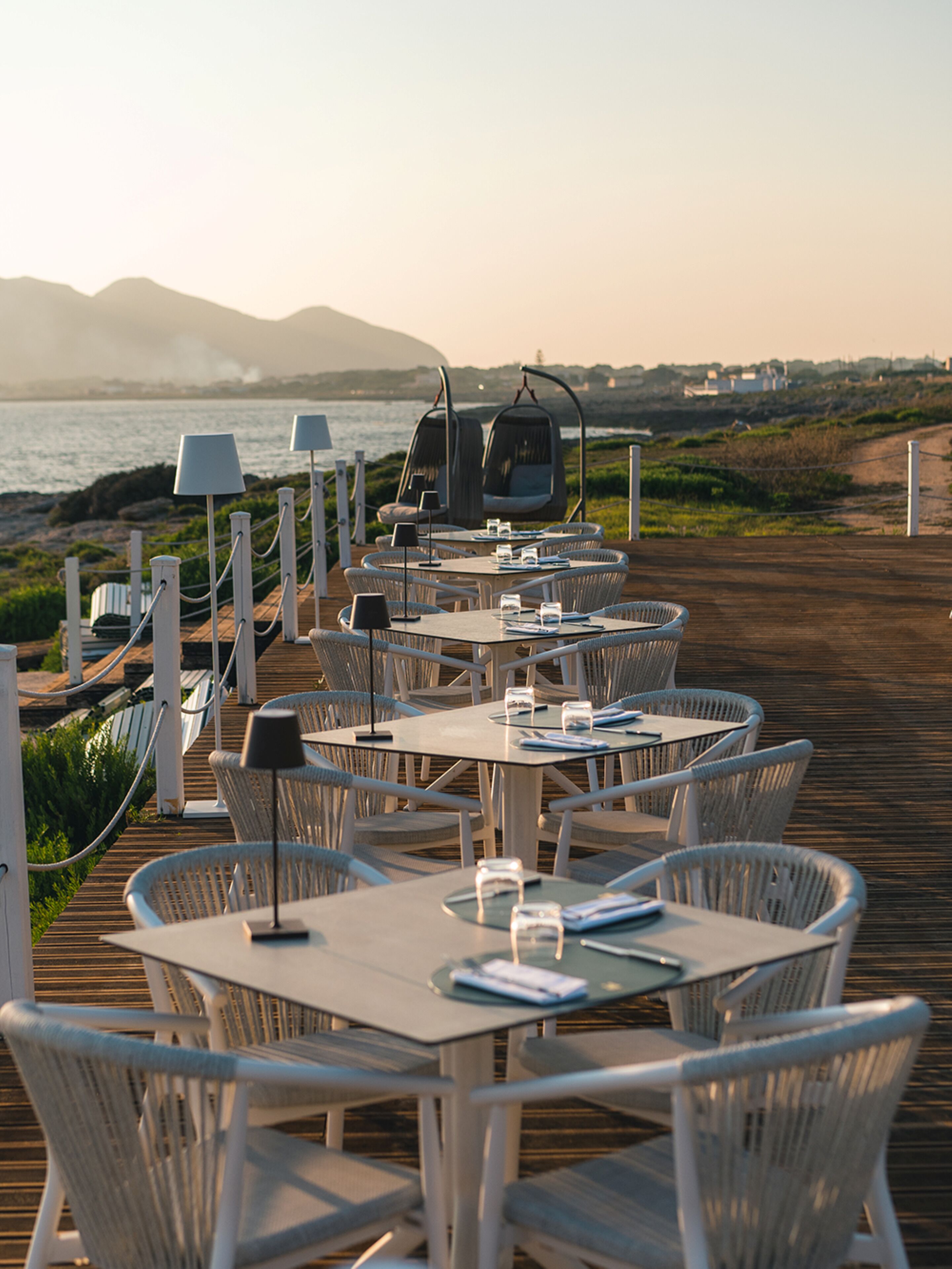A seaside restaurant with outdoor seating, including tables and chairs, and a view of the ocean.