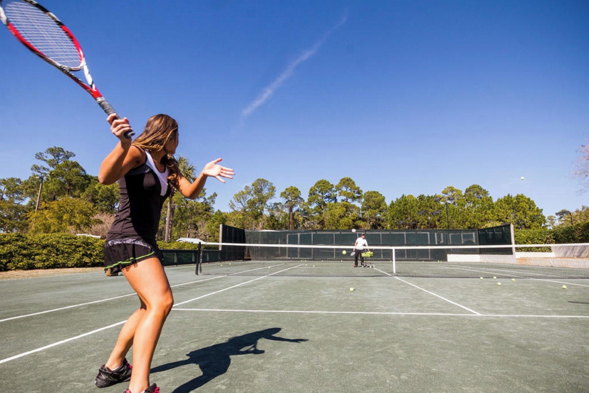 A tennis court with a net, a player in a black outfit, and another player in a white shirt.