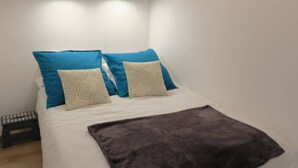 Ein ordentlich gemachtes Bett mit weißer und blauer Bettwäsche, einer braunen Tagesdecke und einem Nachttisch mit Fernbedienung.
