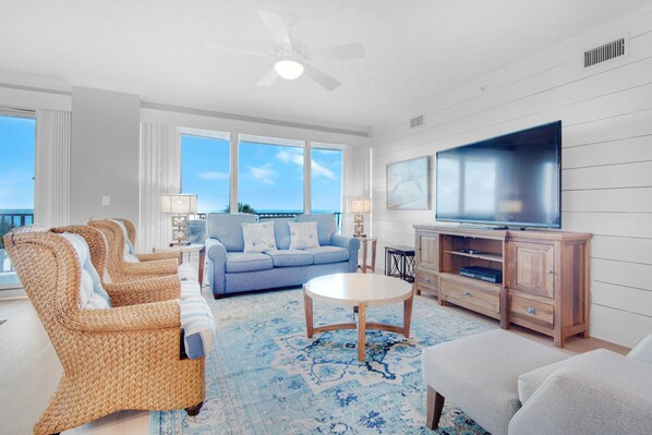 A living room with wicker furniture, a blue sofa, a flat-screen TV, and a view of the ocean.