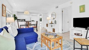 A modern living room with a blue sofa, a glass coffee table, and a TV on a white stand. - 260B - Boca Retreat w/ Pool, Parking, Near Evert Tennis & Shops (Boca Raton)