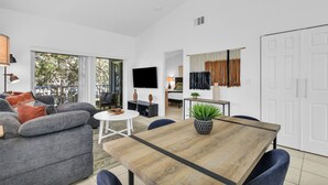A modern living room with a grey sofa, a wooden dining table, and a TV. - 260C - Apt in Boca Raton- Near Evert & Boca Prep (Boca Raton)