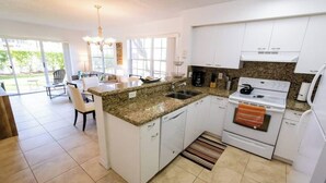 A modern kitchen with white cabinets, granite countertops, a built-in oven, and a dining area with a table and chairs. - 270B - Boca Retreat w/ Pool, Parking, Near Evert Tennis & Shops (Boca Raton)
