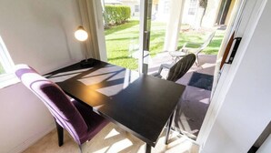 A small, sunlit room with a table and a purple chair, a glass door leading outside, and a view of a lawn and building. - 270B - Boca Retreat w/ Pool, Parking, Near Evert Tennis & Shops (Boca Raton)