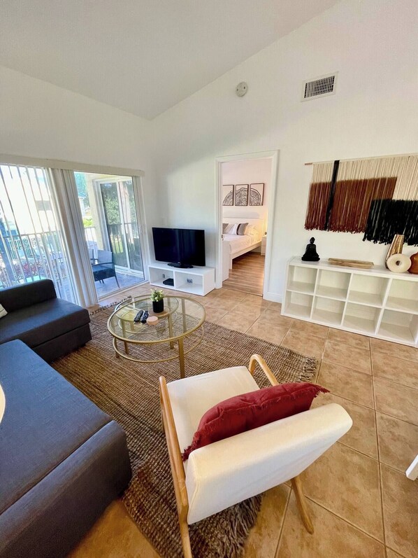 Un salon moderne avec un canapé, une table basse et un téléviseur. Il y a un balcon avec vue.