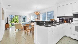 A modern kitchen with white cabinets, a granite countertop, and a dining area with a table and chairs. - 350B - Boca Retreat w/ Pool, Parking, Near Evert Tennis & Shops (Boca Raton)