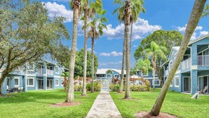 A pathway leading to a row of blue buildings with balconies, surrounded by palm trees and greenery. - 350B - Boca Retreat w/ Pool, Parking, Near Evert Tennis & Shops (Boca Raton)