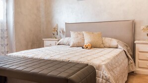 A bedroom with a large bed, a bedside table, a nightstand, and a bench.