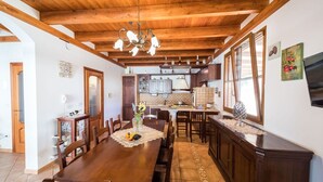 A spacious kitchen with wooden beams, a dining area with a wooden table and chairs, and a view of the outside through large windows.