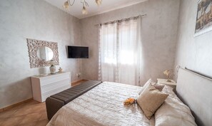 A bedroom with a bed, a dresser, a television, and a window with curtains.