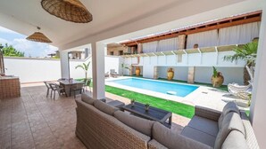 A covered patio with a pool, wicker furniture, and outdoor seating.