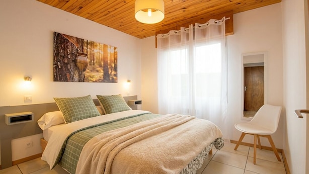 A bedroom with a bed, a chair, a painting, and a window with curtains. - Résidence Amaréna (Saint-Paul-les-Dax)