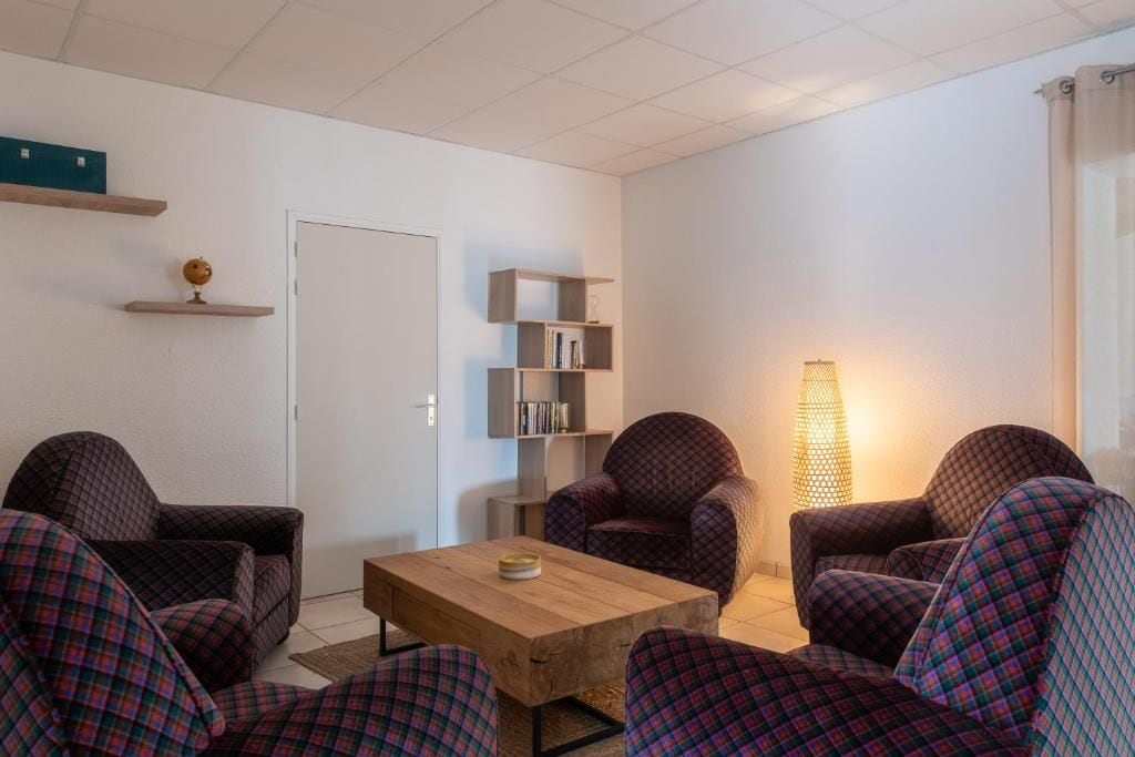 Una sala de estar con una mesa de centro de madera, sillones a cuadros, una estantería y una lámpara de pie.