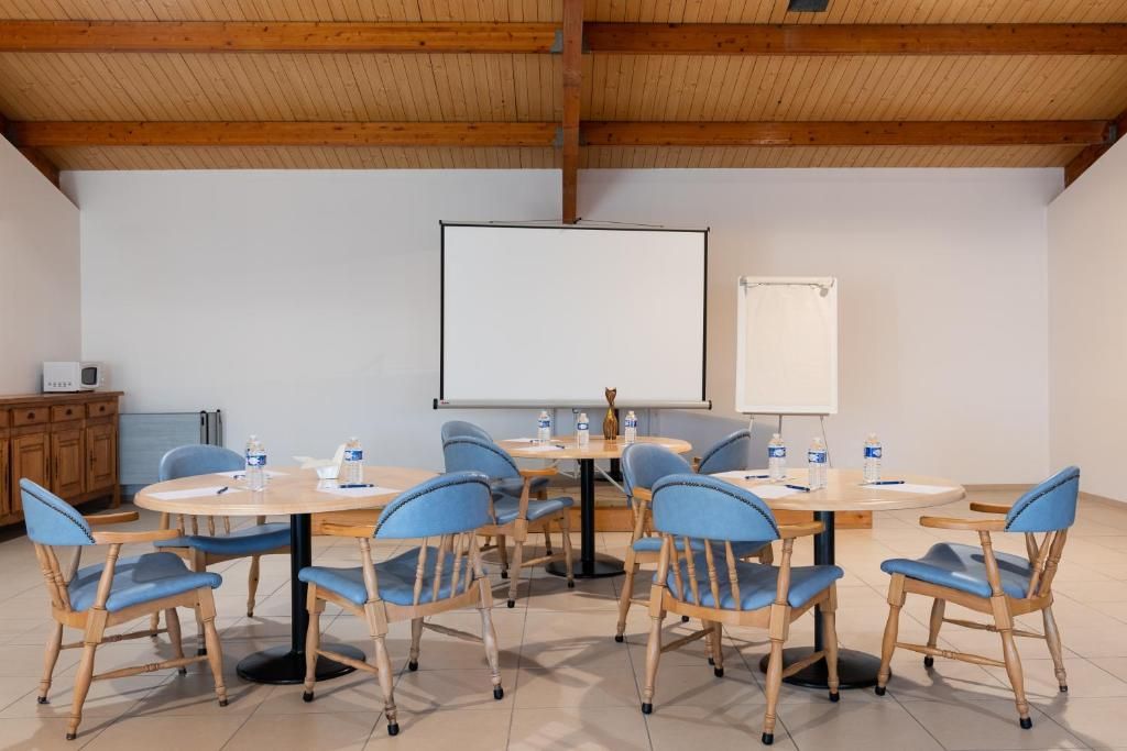 Uma sala de conferências com uma mesa redonda, cadeiras azuis, um quadro branco e uma tela de projetor.