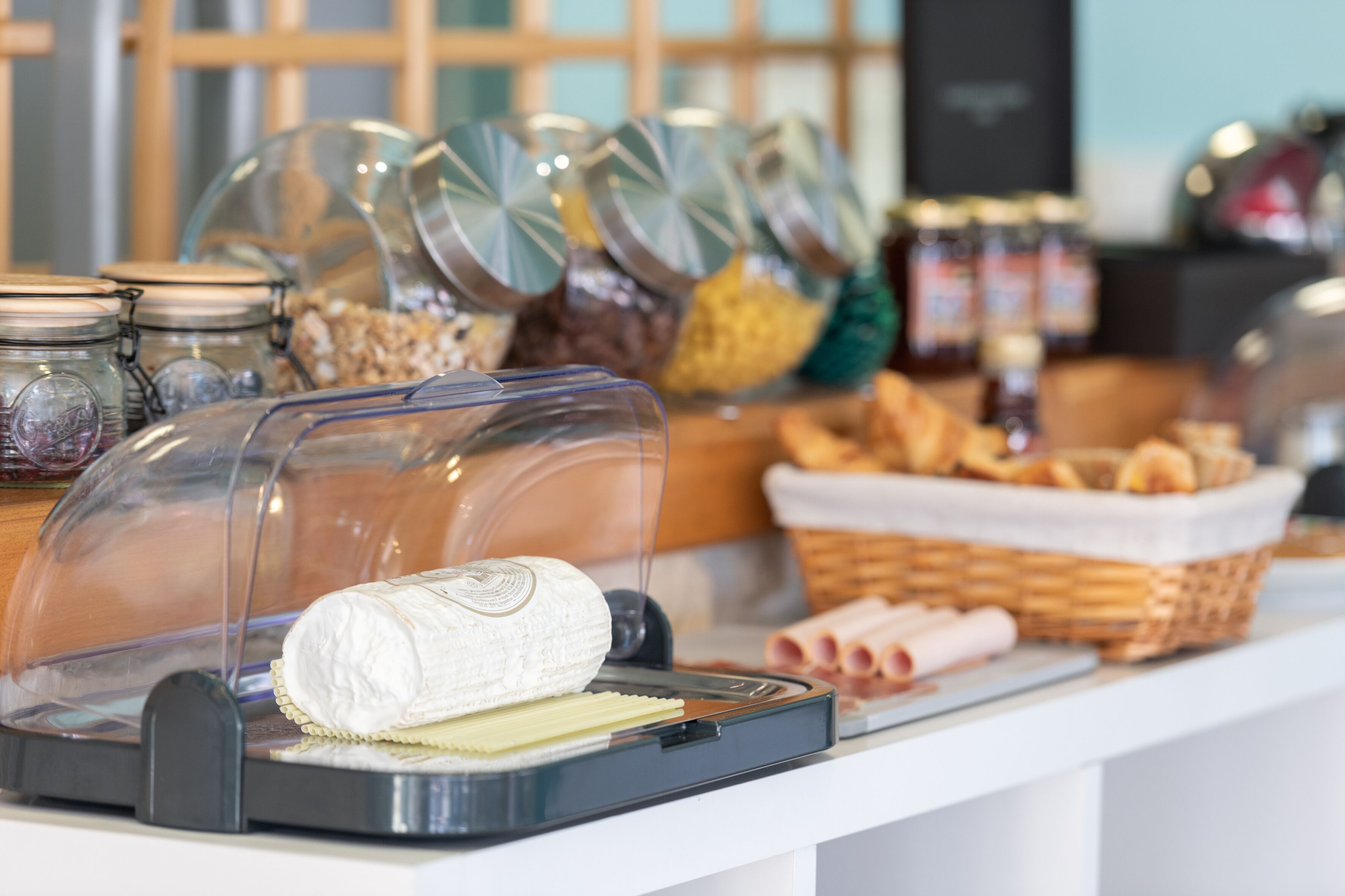 Un buffet con diversi cibi, tra cui un vassoio di formaggi coperto, barattoli di condimenti e cestini di pane.